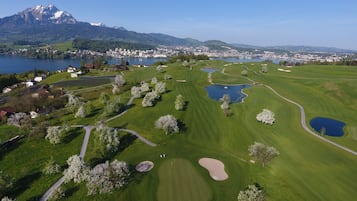 Campo de golf con numerosos peligros de agua, búnkeres de arena y montañas y un lago al fondo.