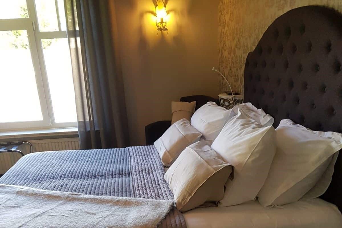A neatly made bed with a white comforter and pillows, a dark upholstered headboard, and a wall-mounted light fixture.