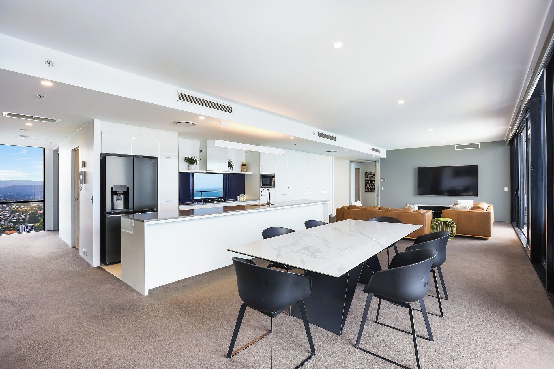 A modern kitchen with a central island, a dining area with a marble table, and a living area with a large TV.
