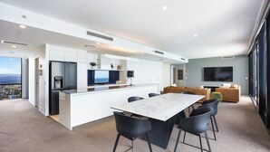 A modern kitchen with a central island, a dining area with a marble table, and a living area with a large TV. - One and Only - Circle on Cavill Sub Penthouse 2672 - 5 bedrooms Level 67 (Gold Coast)
