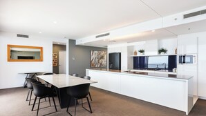 A modern kitchen with white cabinetry, a central island, and a dining area with a marble table and black chairs. - One and Only - Circle on Cavill Sub Penthouse 2672 - 5 bedrooms Level 67 (Gold Coast)