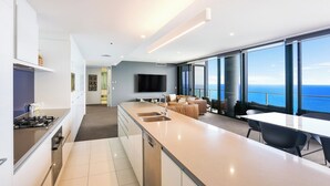 A modern kitchen with a central island, a dining area with a view of the ocean, and a living area with a sofa and a flat-screen TV. - One and Only - Circle on Cavill Sub Penthouse 2672 - 5 bedrooms Level 67 (Gold Coast)