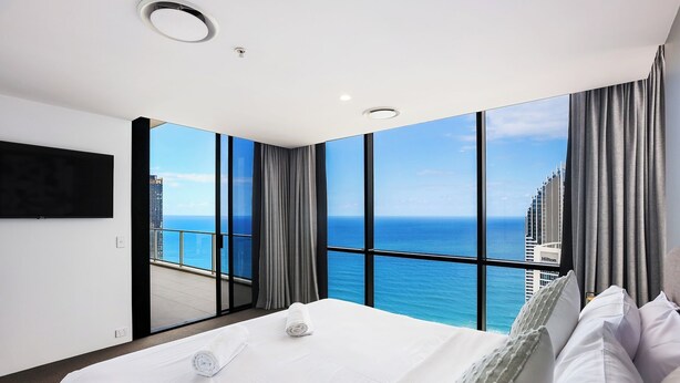 A hotel room with a large bed, a TV, and a view of the ocean and city skyline. - One and Only - Circle on Cavill Sub Penthouse 2672 - 5 bedrooms Level 67 (Gold Coast)