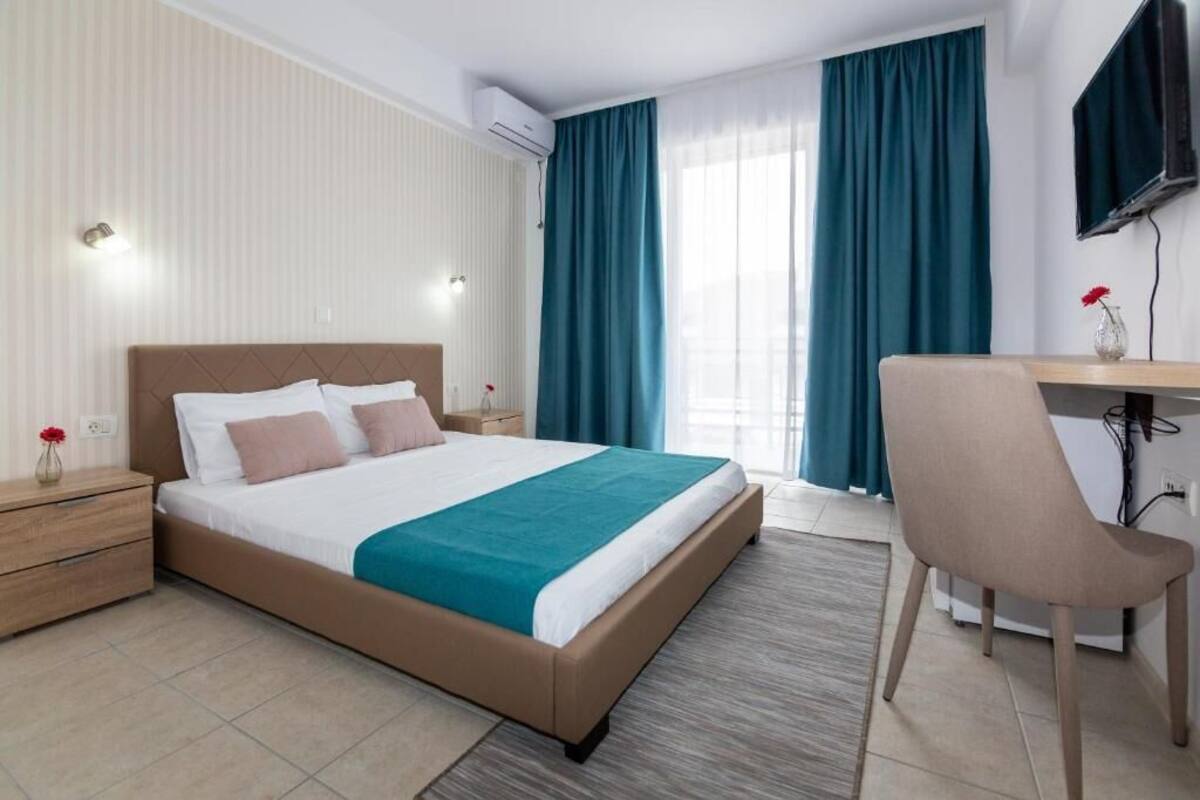 Habitación de hotel con cama, escritorio, silla, televisión y ventana con cortinas.
