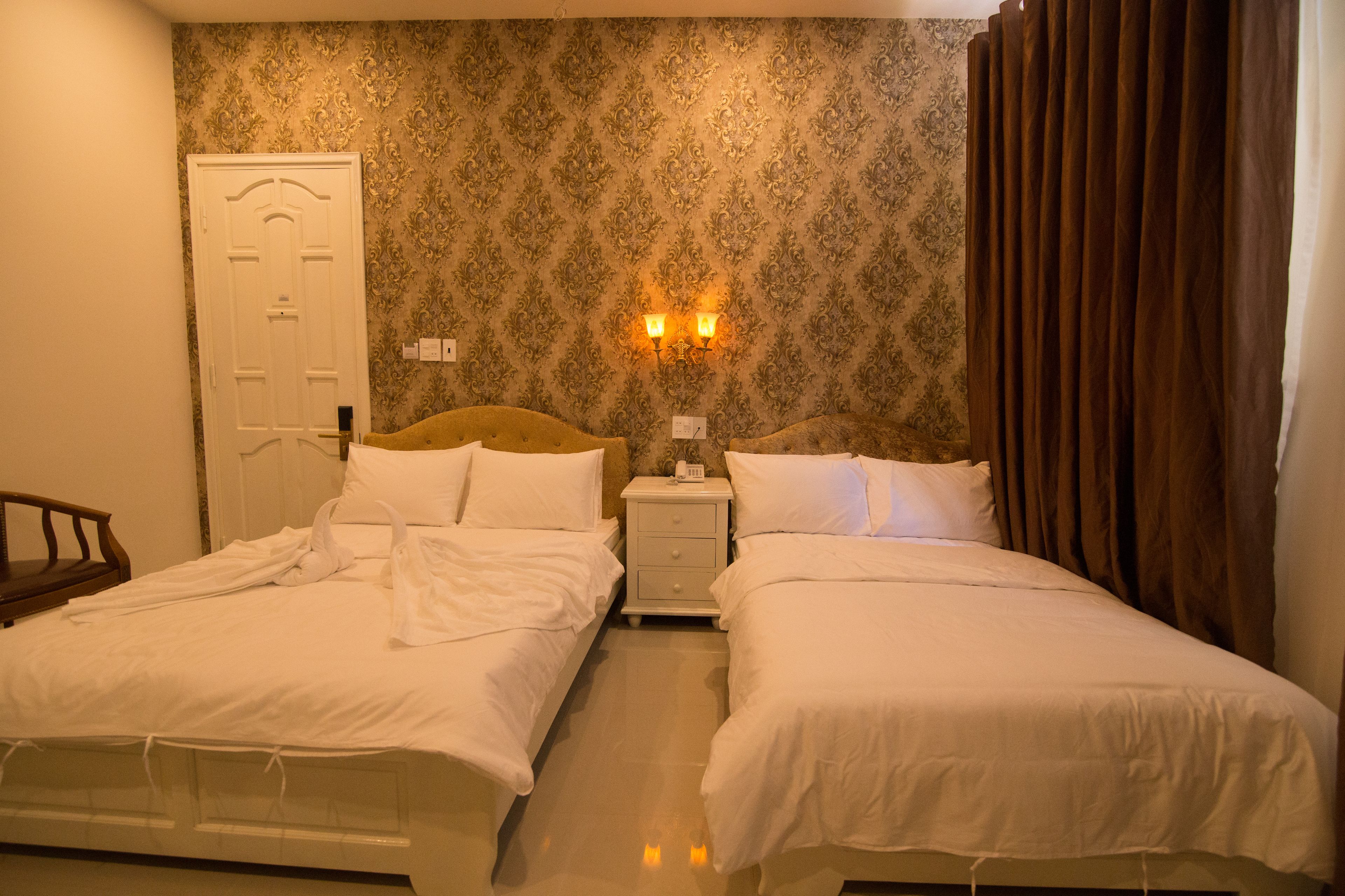 Une chambre d’hôtel avec deux lits, une porte blanche, une table de chevet avec une lampe et un papier peint à motifs.