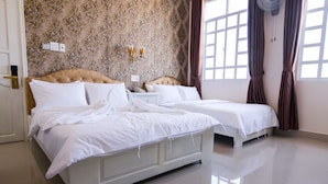 Una cama doble con ropa de cama blanca, una mesita de noche con lámpara y una pared con papel tapiz decorado.