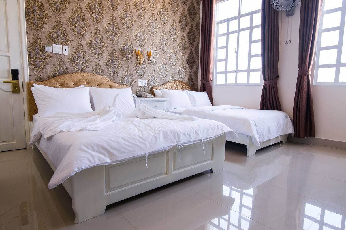 A double bed with white linens, a bedside table with a lamp, and a wall with ornate wallpaper.