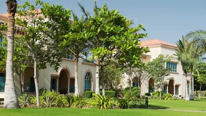 A large, multi-story building with arched windows and a red-tiled roof, surrounded by well-maintained lawns and palm trees. - Al Raha Beach Hotel Villas (Abu Dhabi)