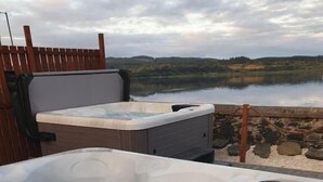 A hot tub with a wooden deck and a view of a lake and hills in the background. - The Grey Gull Hotel (Lochgilphead)