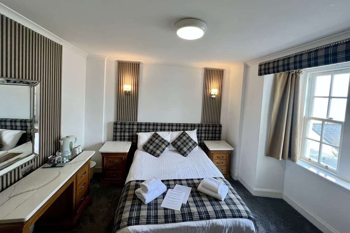 Une chambre d’hôtel avec un lit, un bureau, un miroir et une fenêtre avec des rideaux.
