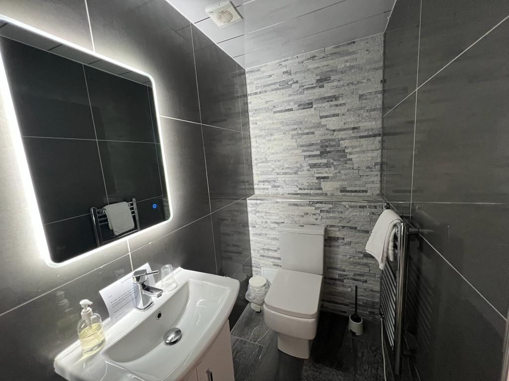 A modern bathroom with a large mirror, white sink, and a toilet.