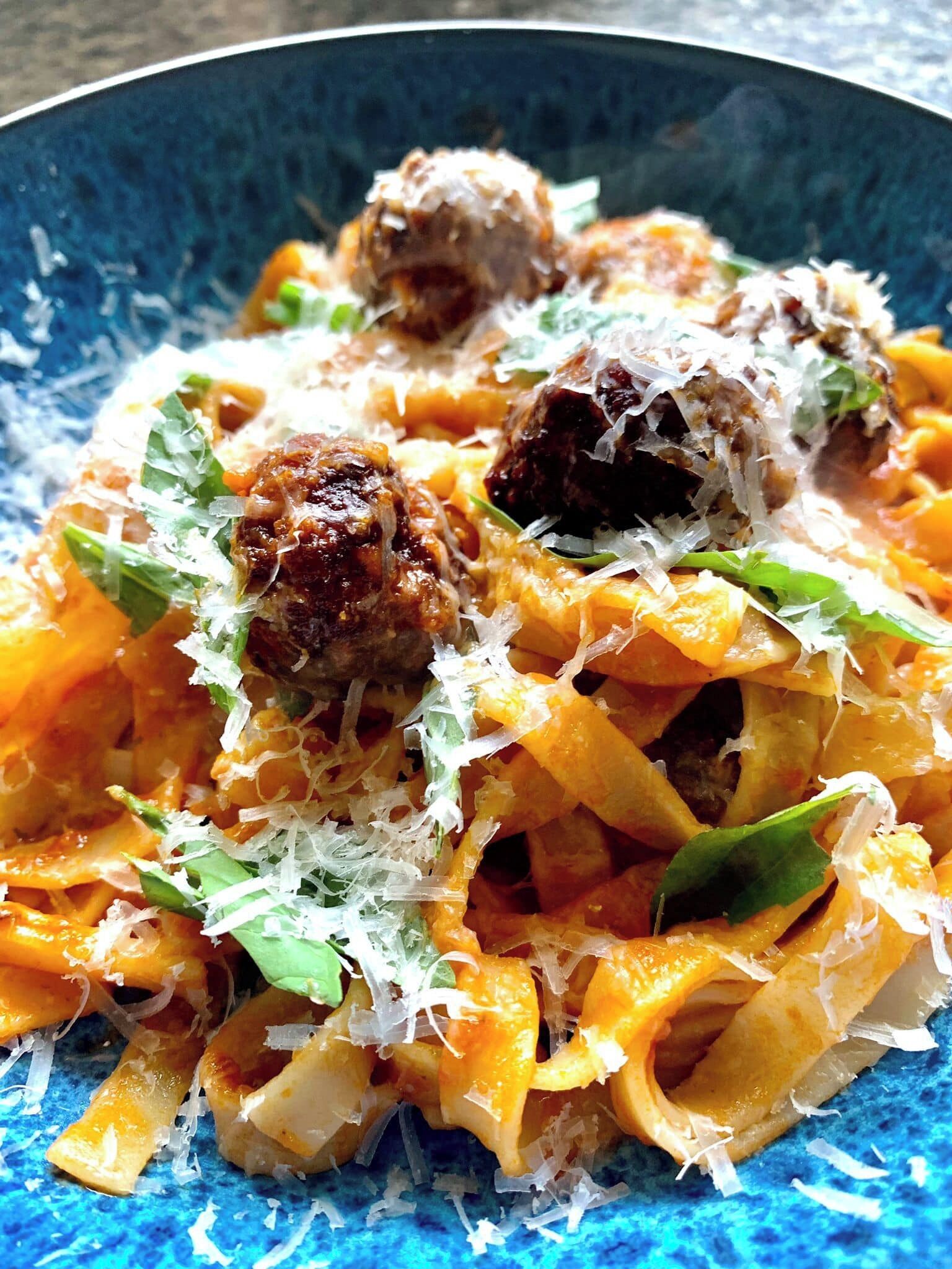A bowl of pasta with meatballs and grated cheese.
