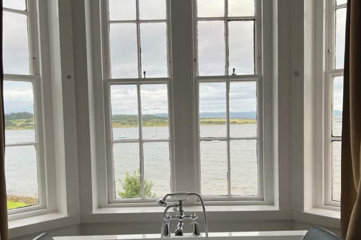 Une salle de bain avec une baignoire et une vue sur un lac, grâce à de grandes fenêtres.
