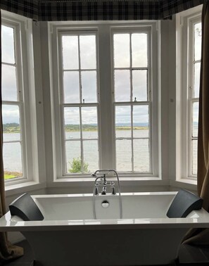 A bathroom with a bathtub and a view of a lake through large windows. - The Grey Gull Hotel (Lochgilphead)