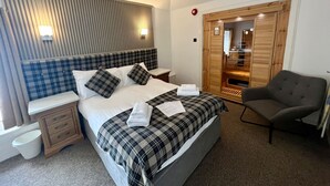 A modern hotel room with a large bed, a wooden wardrobe, a chair, and a bedside table. - The Grey Gull Hotel (Lochgilphead)