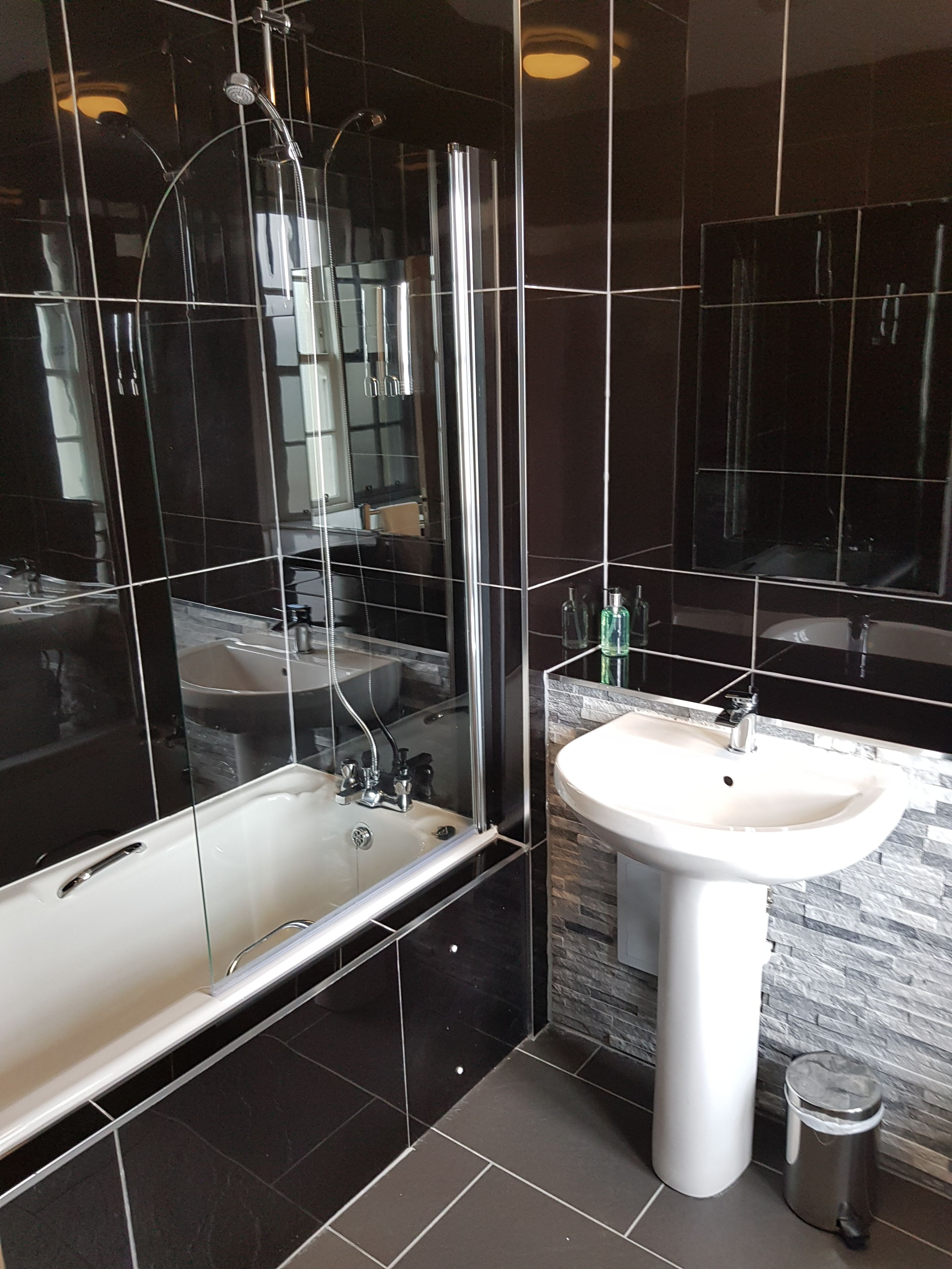 Un baño moderno con ducha envuelta en vidrio, un lavamanos blanco y pared revestida de mármol.