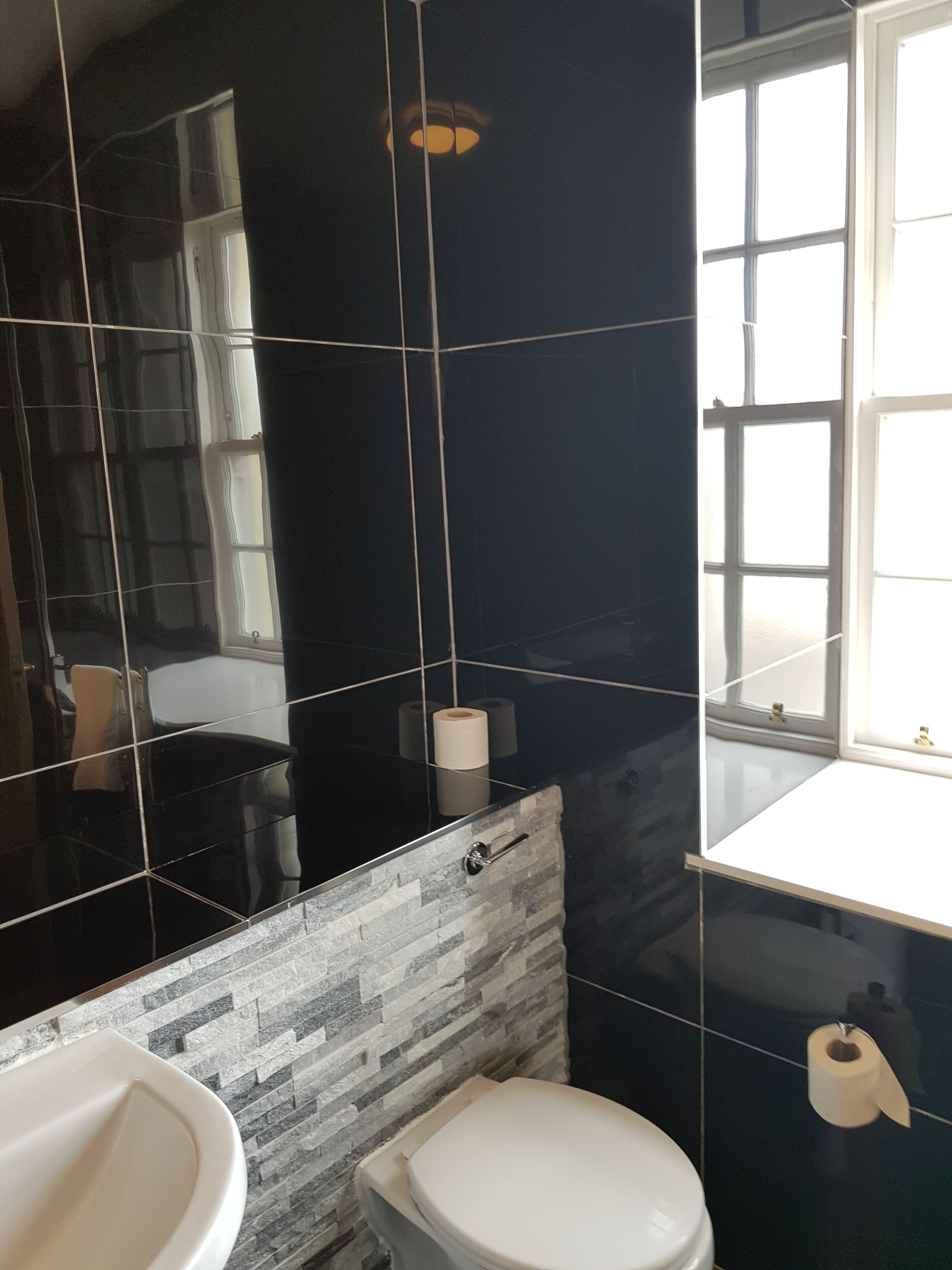 Ein Badezimmer mit schwarzem Fliesenwand, einem weißen Waschbecken und einer Toilette.