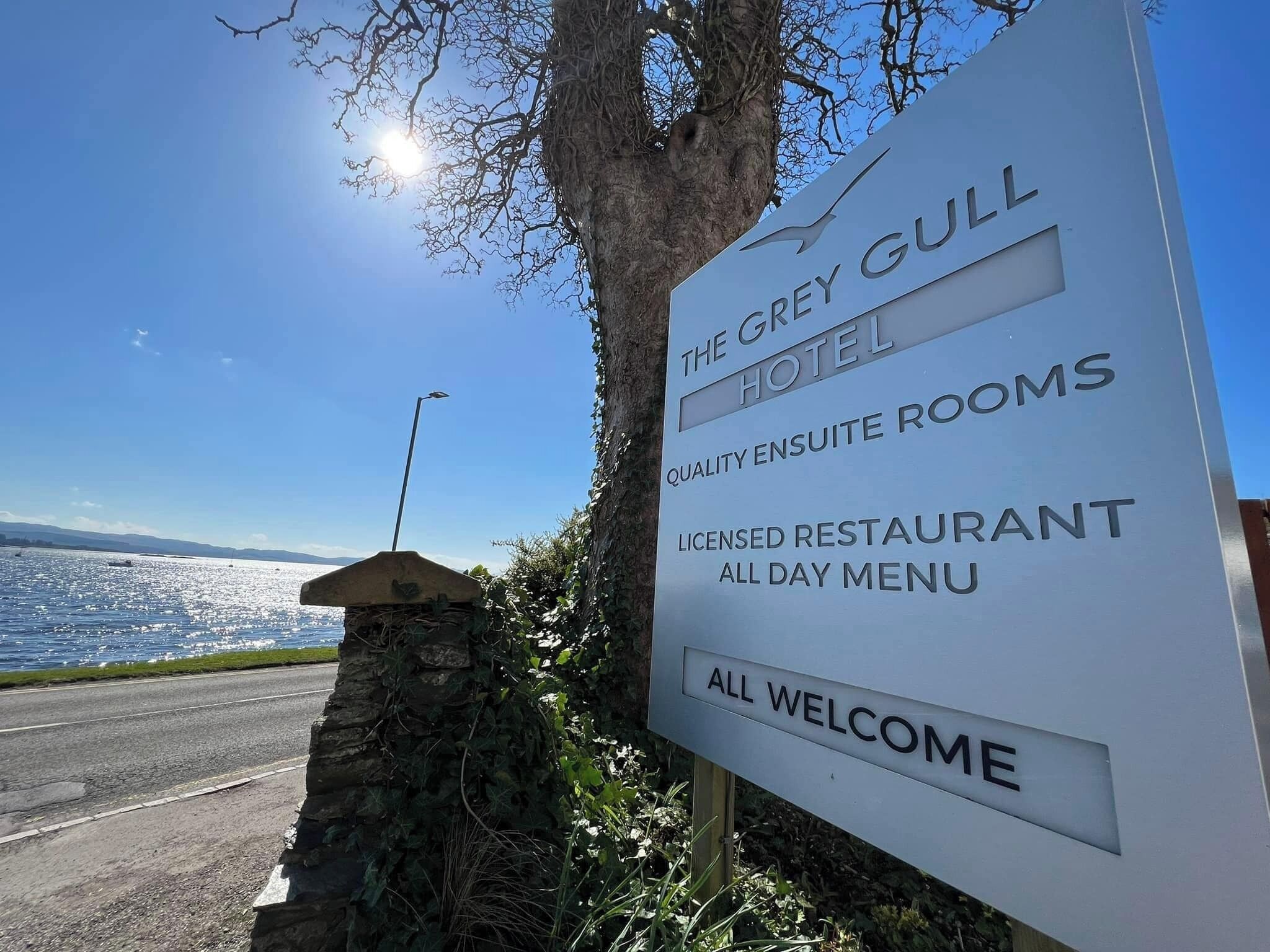 Segnaletica dell'Hotel Grey Gull, che indica la presenza di camere singole di qualità, un ristorante con licenza e menu disponibile tutto il giorno, e accoglie tutti gli ospiti.