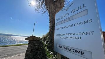 Une enseigne indique l’hôtel The Grey Gull, précisant qu’il propose des chambres de qualité avec salle de bains privative, un restaurant agréé servant des plats toute la journée, et qu’il accueille tous les clients.