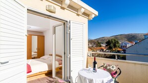 A balcony with a table, chairs, and a bed with a view of a hillside. - Nikola Apartments (Dubrovnik)