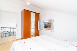 Um quarto com cama, guarda-roupa, janela e varanda com guarda-corpo.