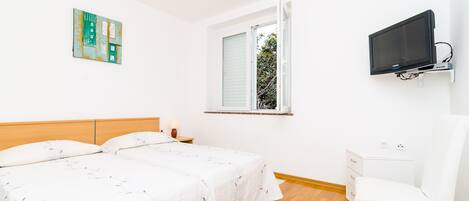 A bedroom with two beds, a TV mounted on the wall, a window, and a chair.