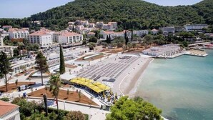 A coastal town with a beach, buildings, and a hill in the background. - Nikola Apartments (Dubrovnik)