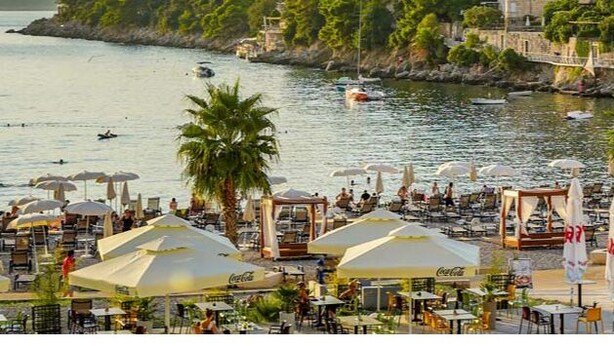 A coastal area with outdoor seating and umbrellas, a stone building, and a bridge over the water. - Nikola Apartments (Dubrovnik)