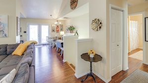 A spacious living room with a dark-colored sofa, a dining area with a table and chairs, a small side table with a vase, and a hallway leading to a bathroom. - Bitterroot Mountain Views: Montana Family Home! (Hamilton)