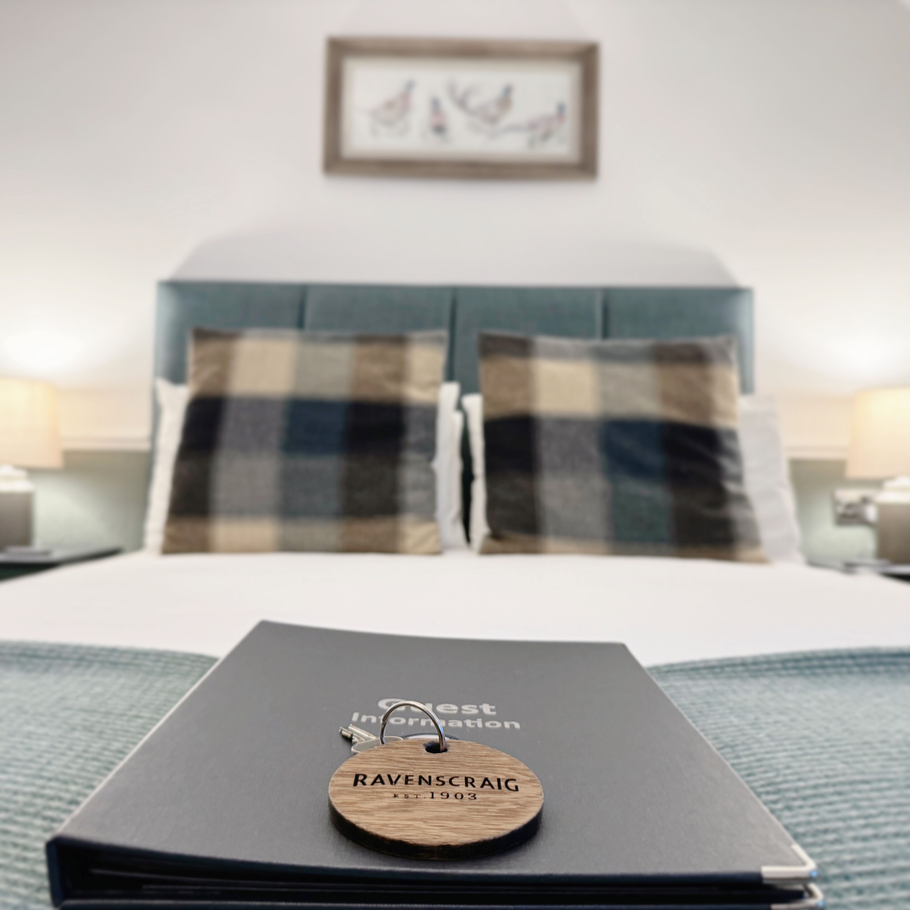 A neatly made bed with plaid bedding, a wooden name tag on the bed, and a framed picture on the wall.