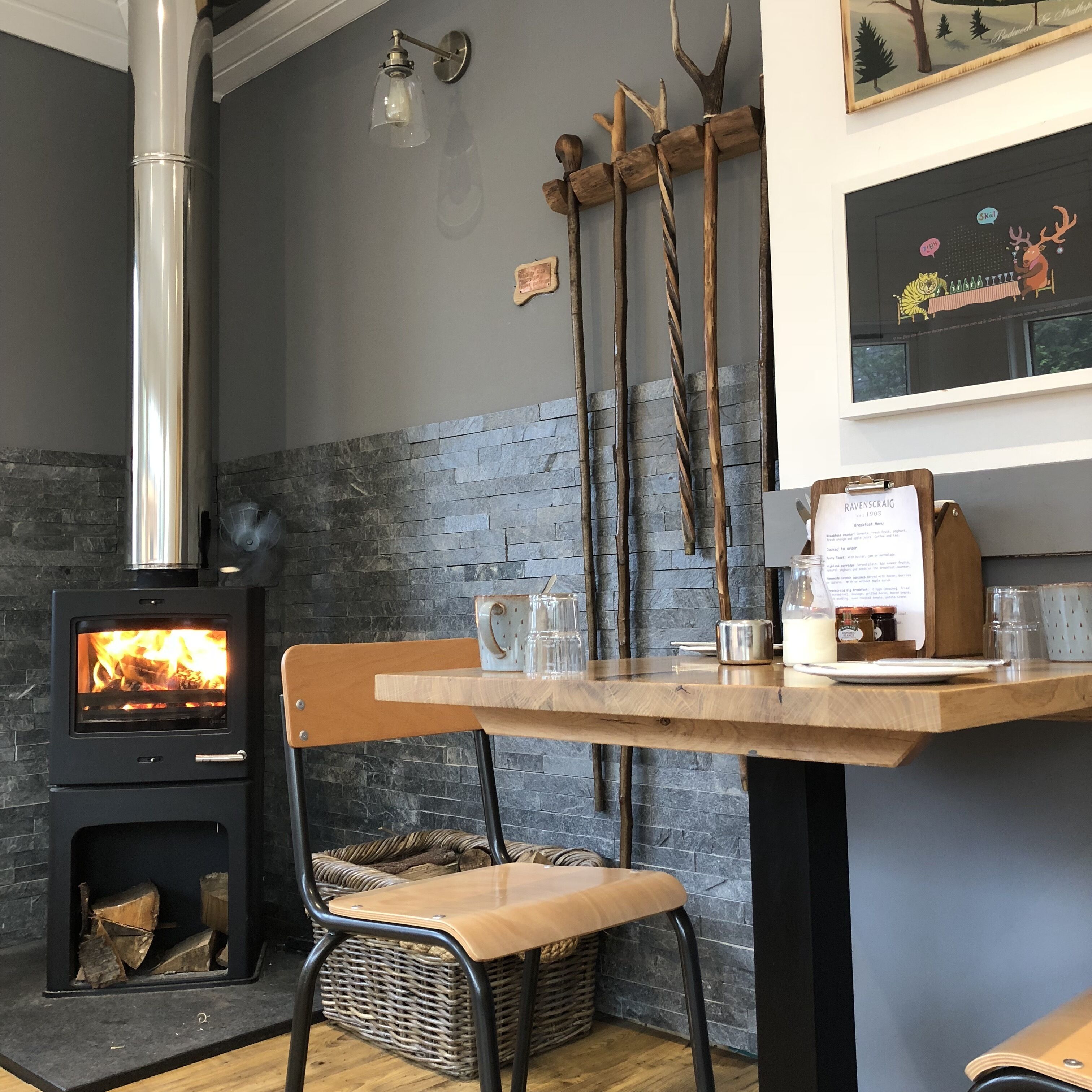A cozy room with a wood-burning stove, a table with chairs, and a wall-mounted light fixture.