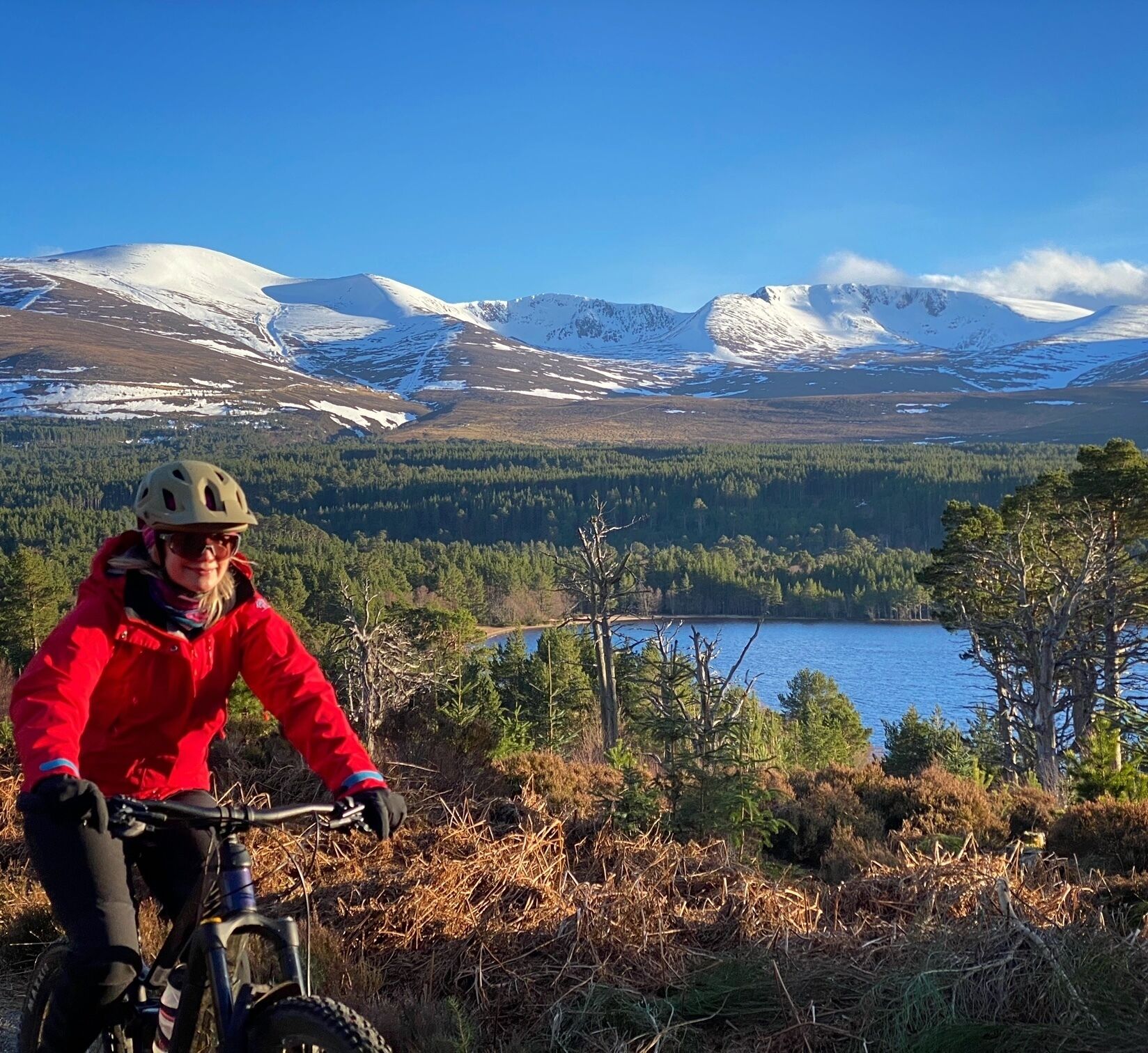 A person riding a mountain bike on a trail with a lake and mountains in the background.