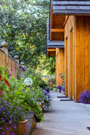 A wooden building with a covered walkway surrounded by lush greenery and potted plants. - Ravenscraig Guest House (Aviemore)