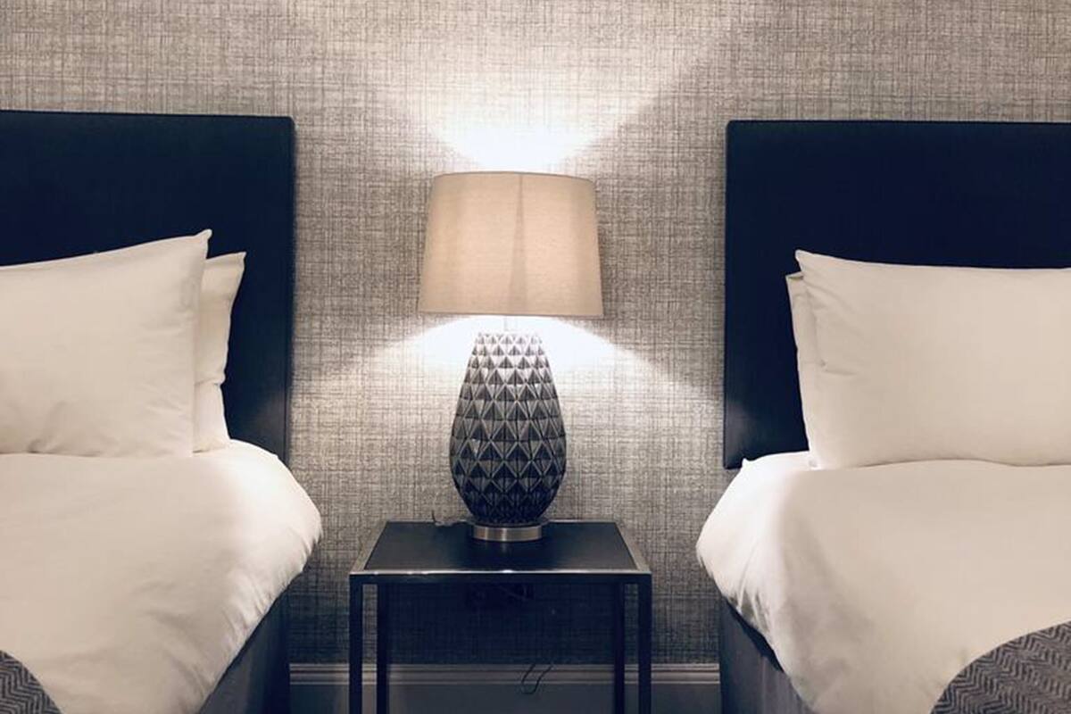 Una habitación de hotel con dos camas, una mesita de noche y una lámpara entre ellas.