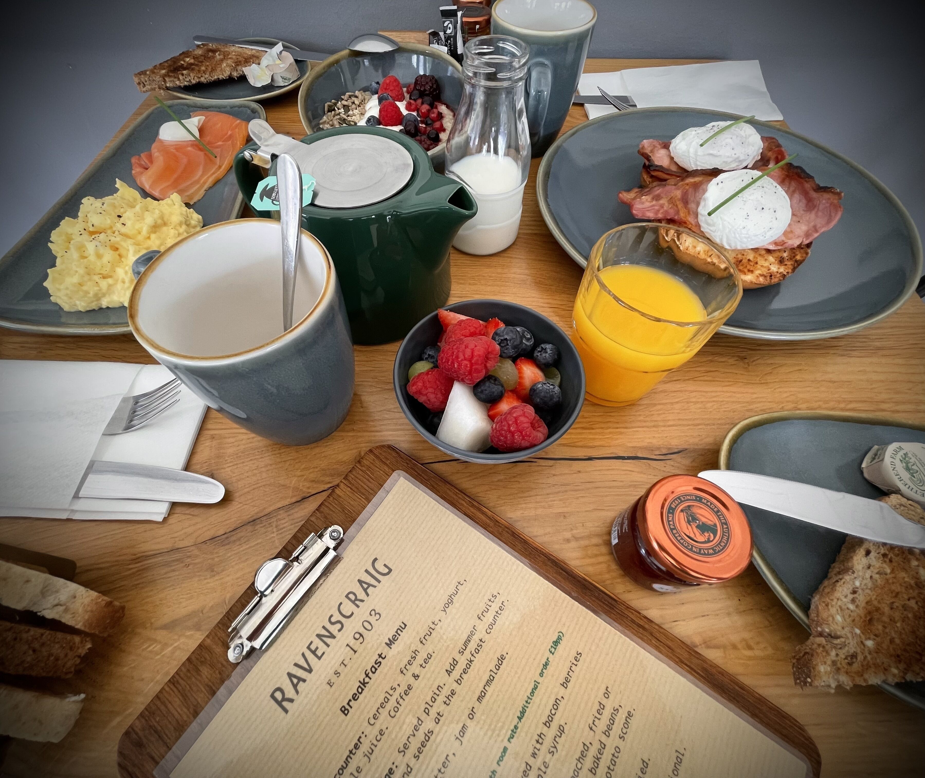 A breakfast spread with various dishes, a menu, and a glass of orange juice on a wooden table.