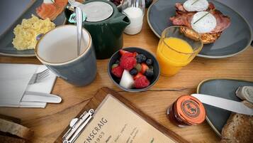A breakfast spread with various dishes, a menu, and a glass of orange juice on a wooden table.