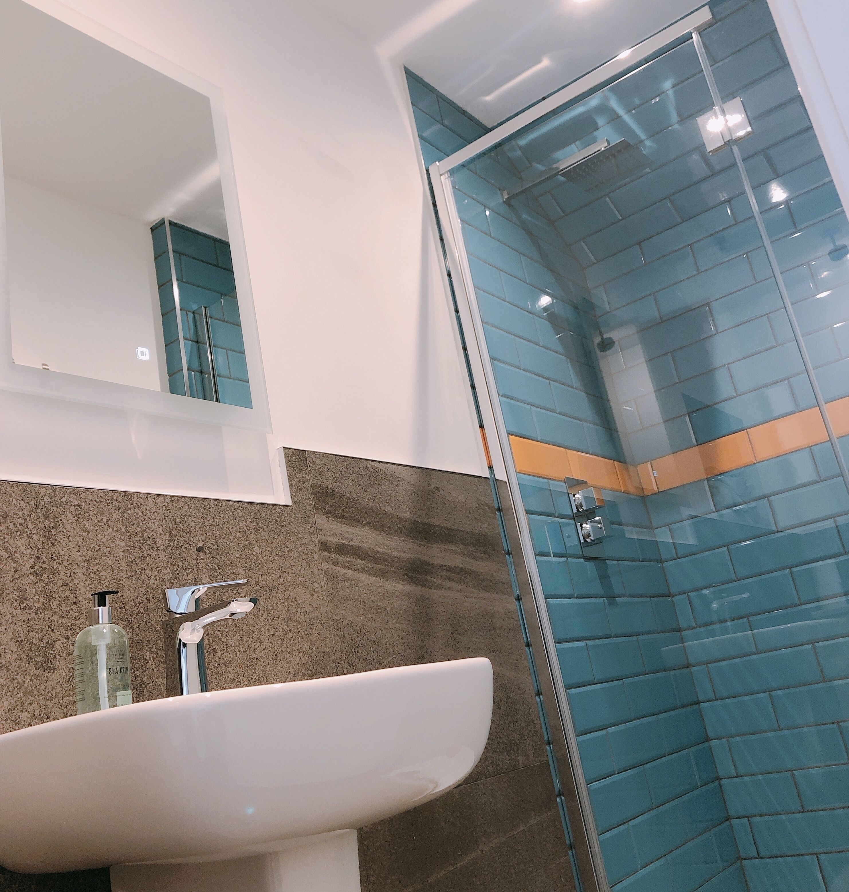 Une salle de bain avec un lavabo blanc, un miroir et une douche en verre avec des carreaux bleus.