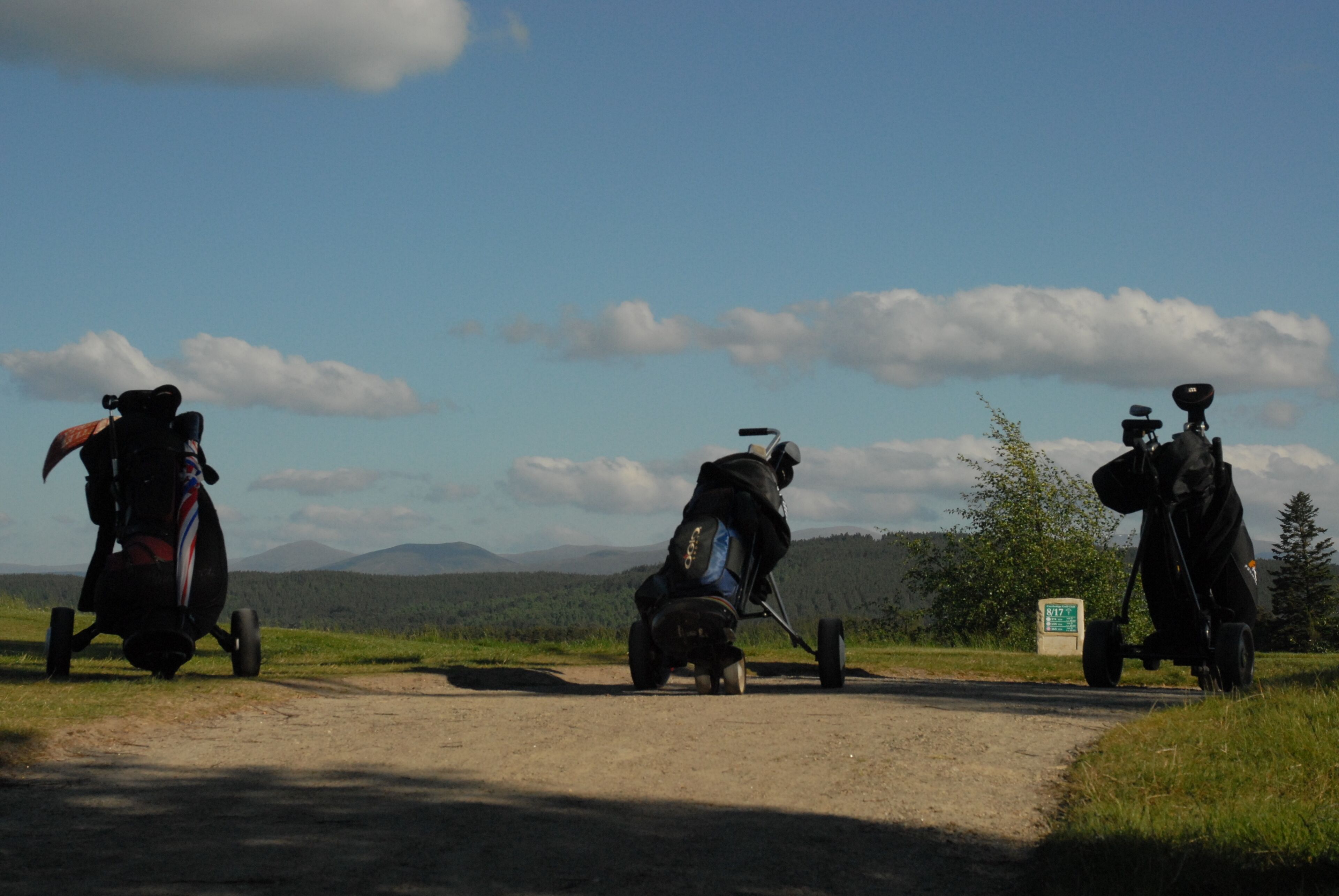 A dirt road with three golf carts parked on the side.