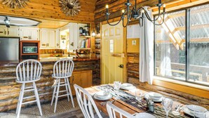 Interior rústico de una cabaña de madera con comedor, cocina y ventanas grandes.