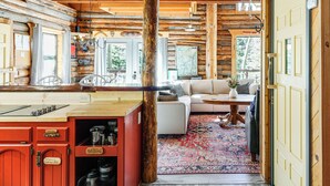 Interior rústico de una cabaña con una zona de comedor de madera, un sofá y una alfombra grande.