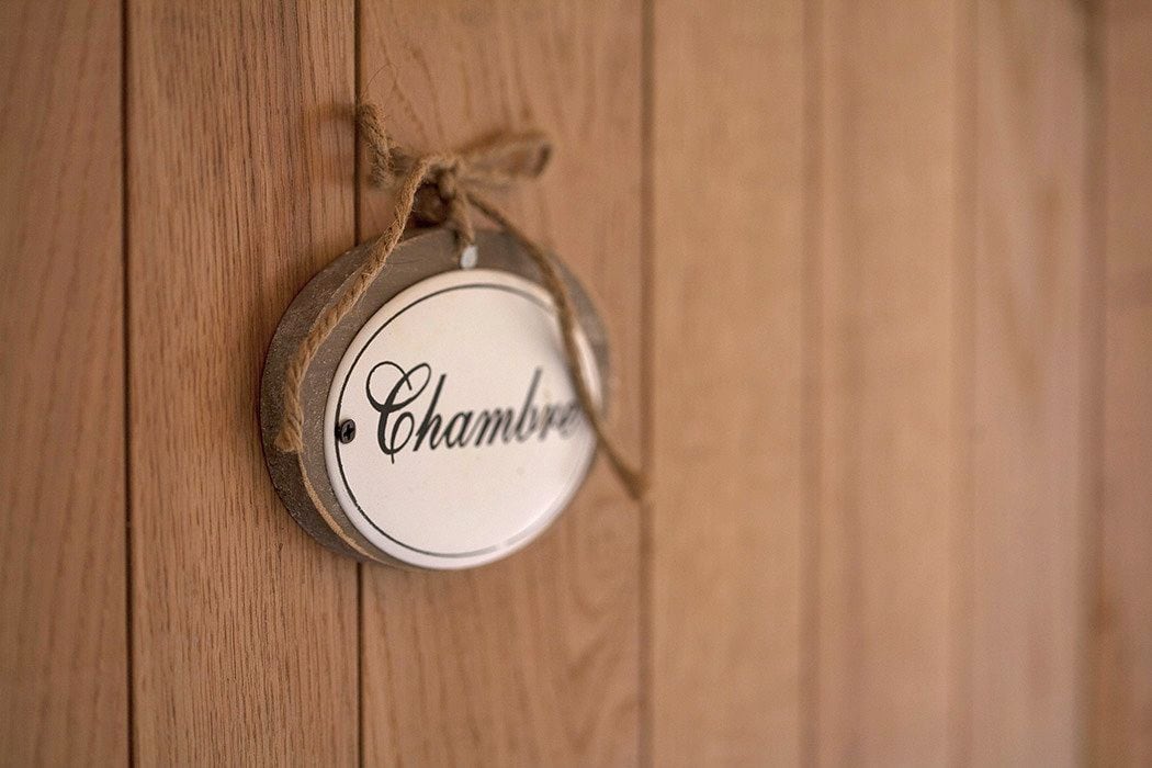 A round, wooden sign with the word "Chambre" on it, hanging on a wooden surface.