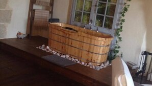A rustic bathroom with a wooden bathtub, a stone wall, and a window with ivy. - Logis De Riparfonds (Bressuire)
