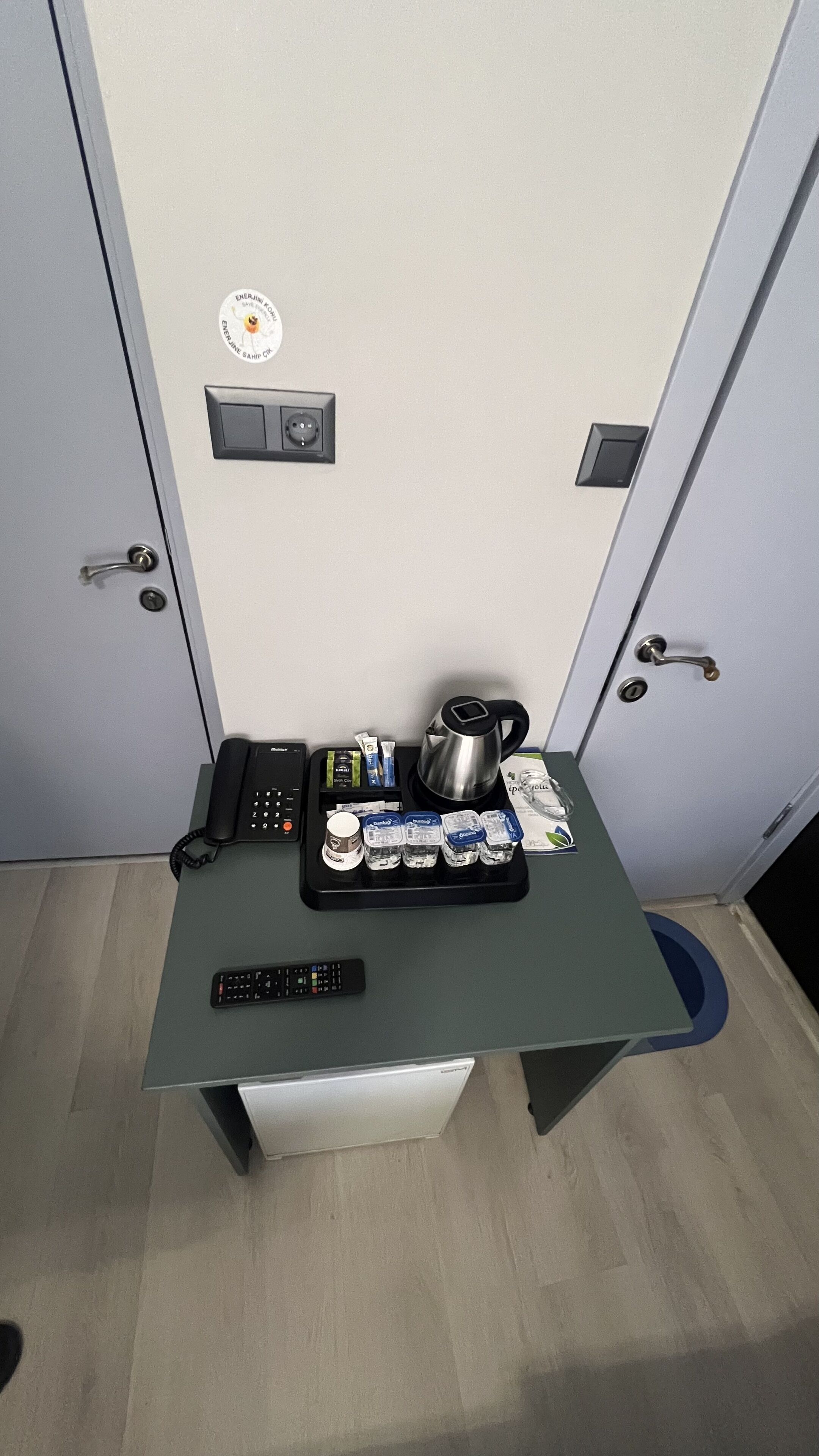 A small table with a phone, remote control, kettle, coffee cups, and toiletries.