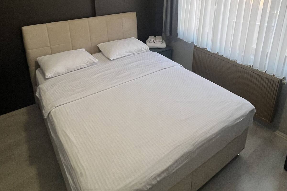 A modern hotel room with a large bed, a bedside table, a lamp, and a window with curtains.