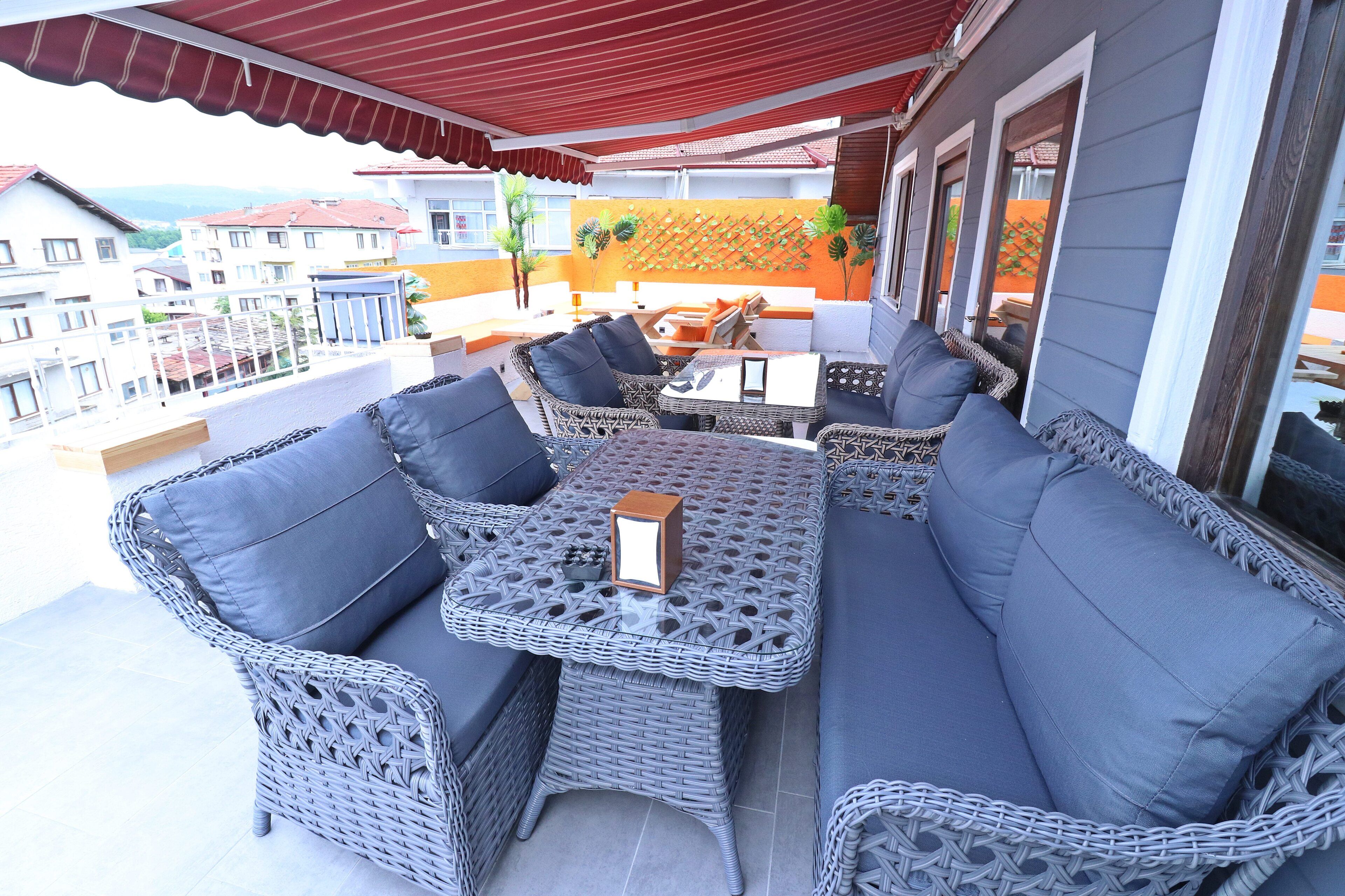 Un balcon doté de meubles en osier, notamment des canapés et une table, et surmonté d’une marquise rouge.