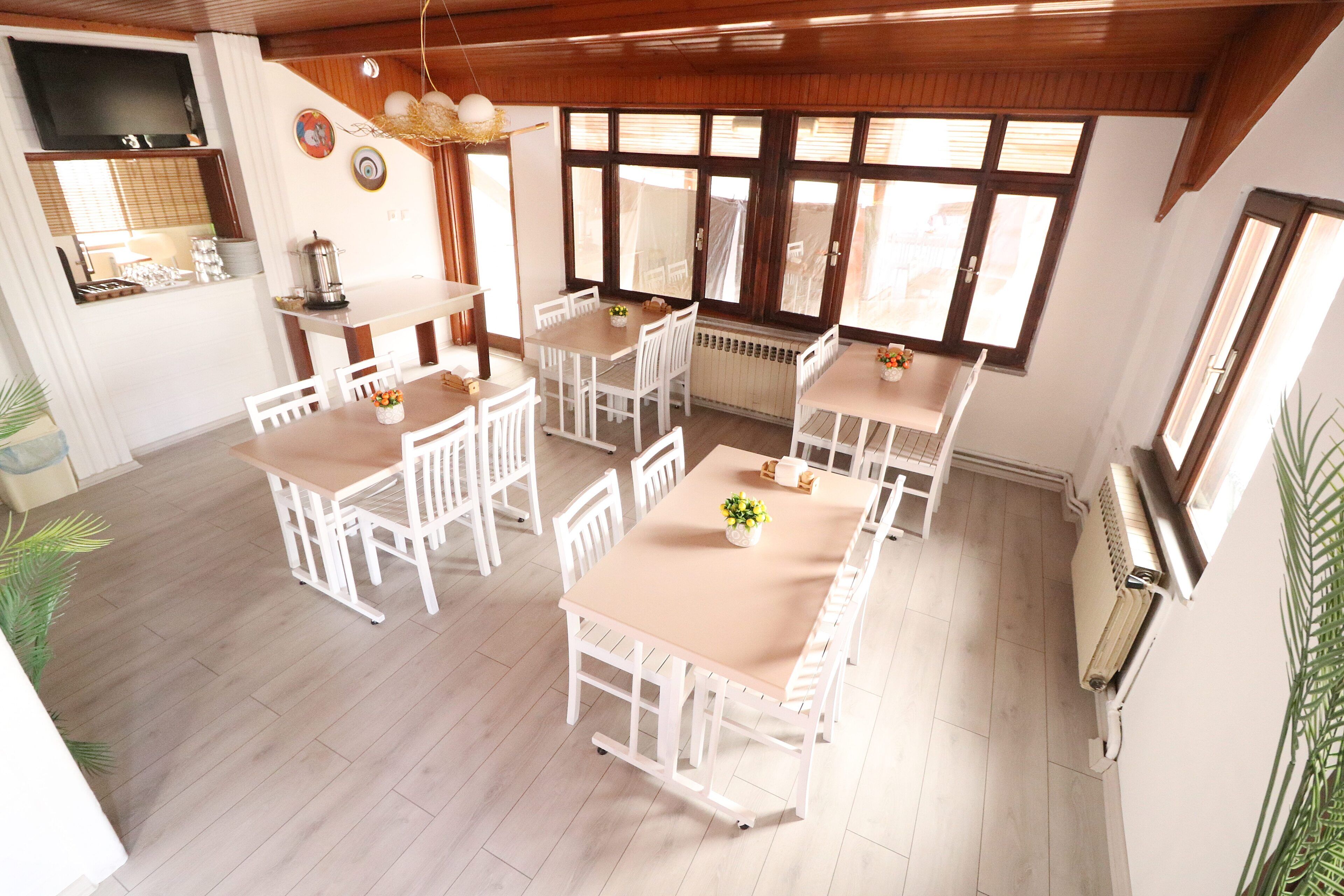 A dining area with white tables and chairs, a kitchen area with a stove and sink, and large windows providing natural light.