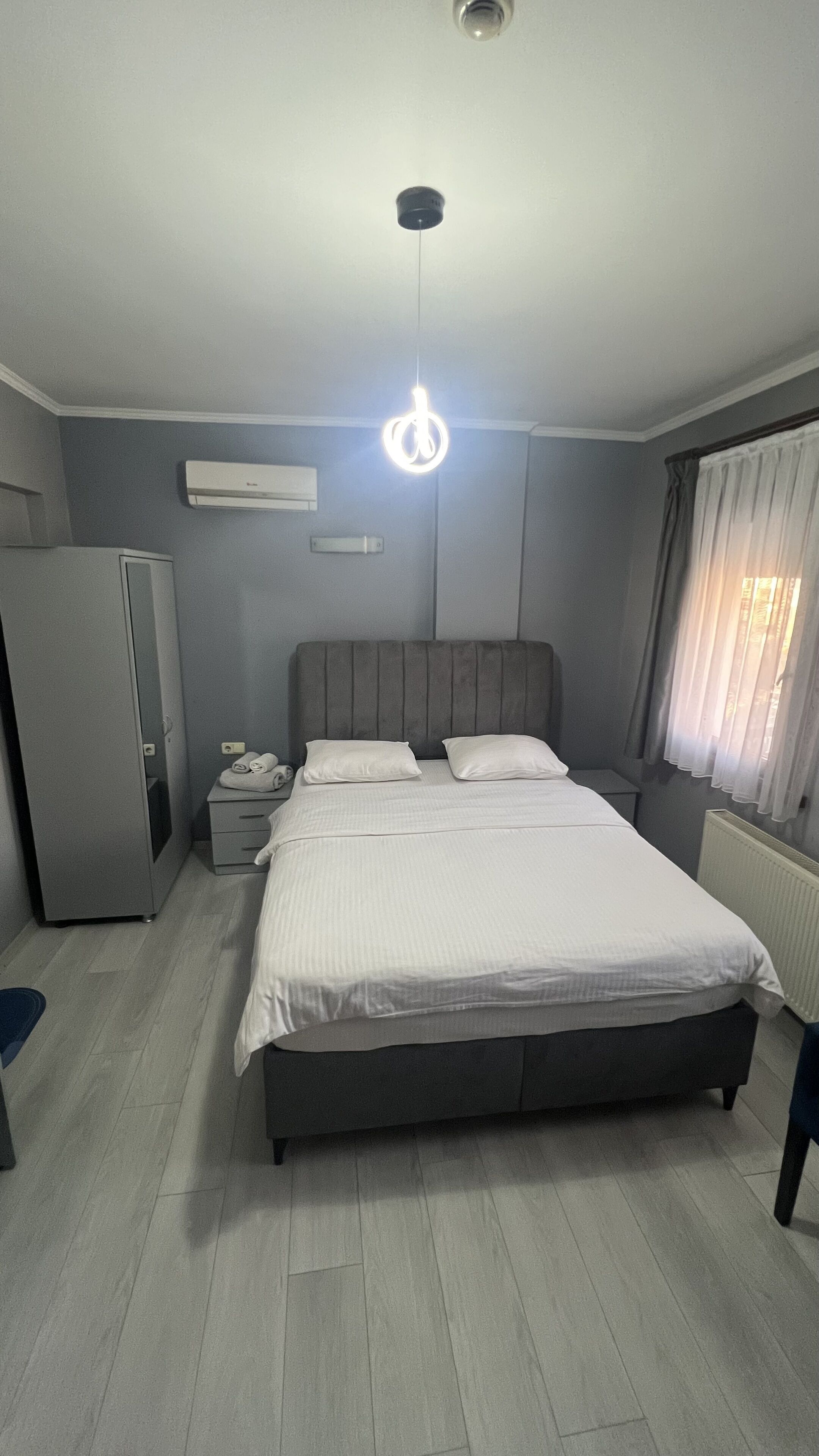 A bedroom with a bed, a nightstand, a wardrobe, an air conditioner, and a window with curtains.