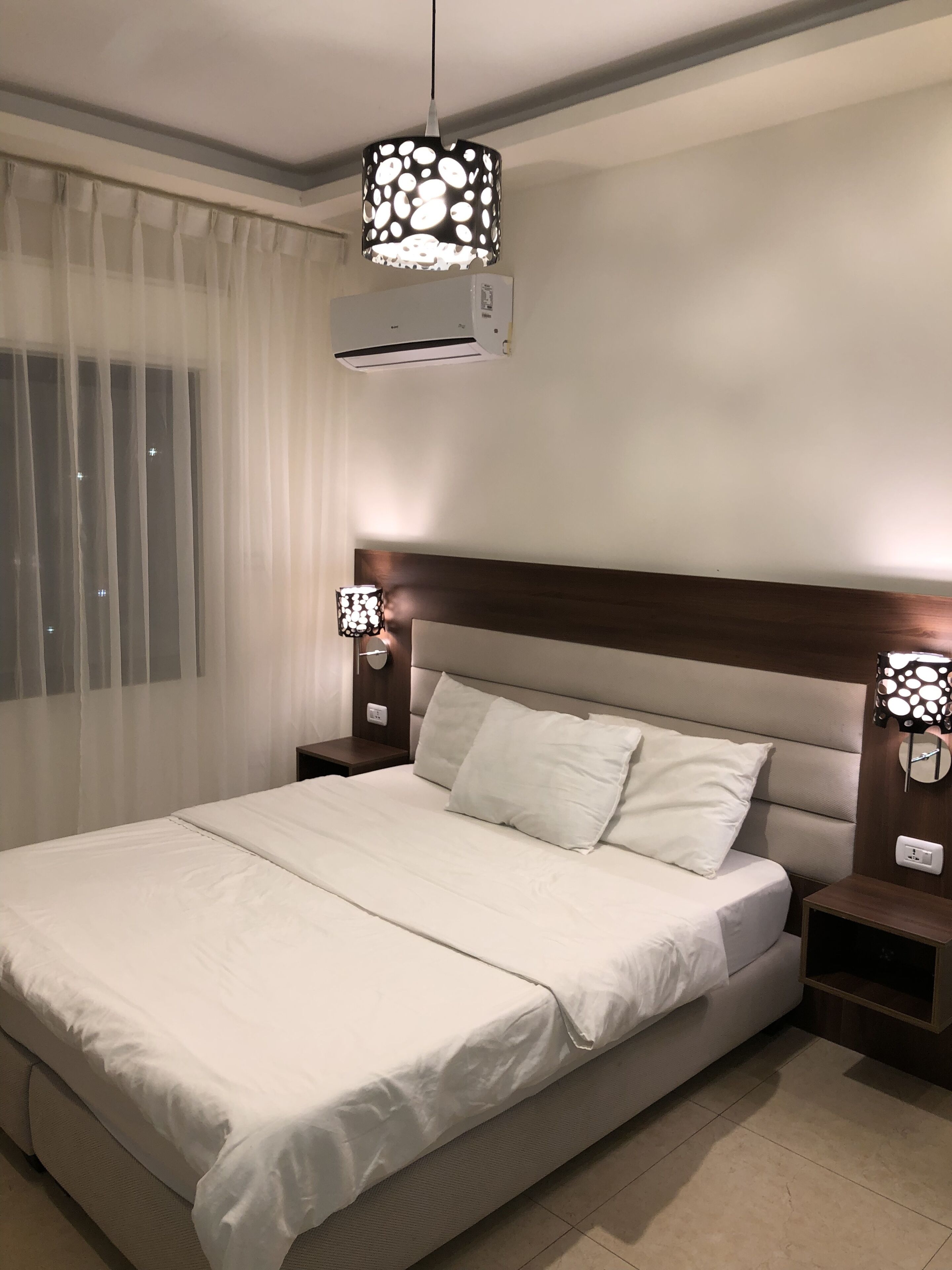 A neatly made bed with white linens, a wooden headboard, and two bedside tables with lamps.
