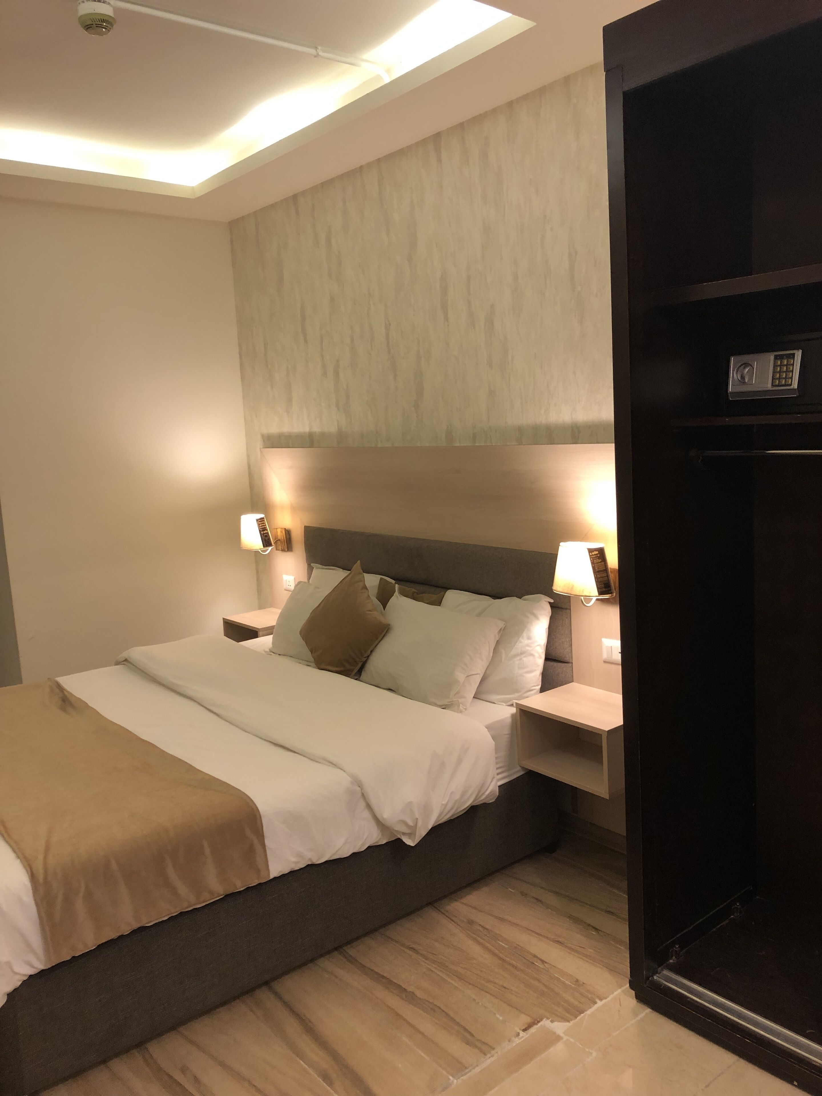 Een moderne hotelkamer met een groot bed, twee nachtkastjes met lampen, een inbouwkast en een plafondlamp.