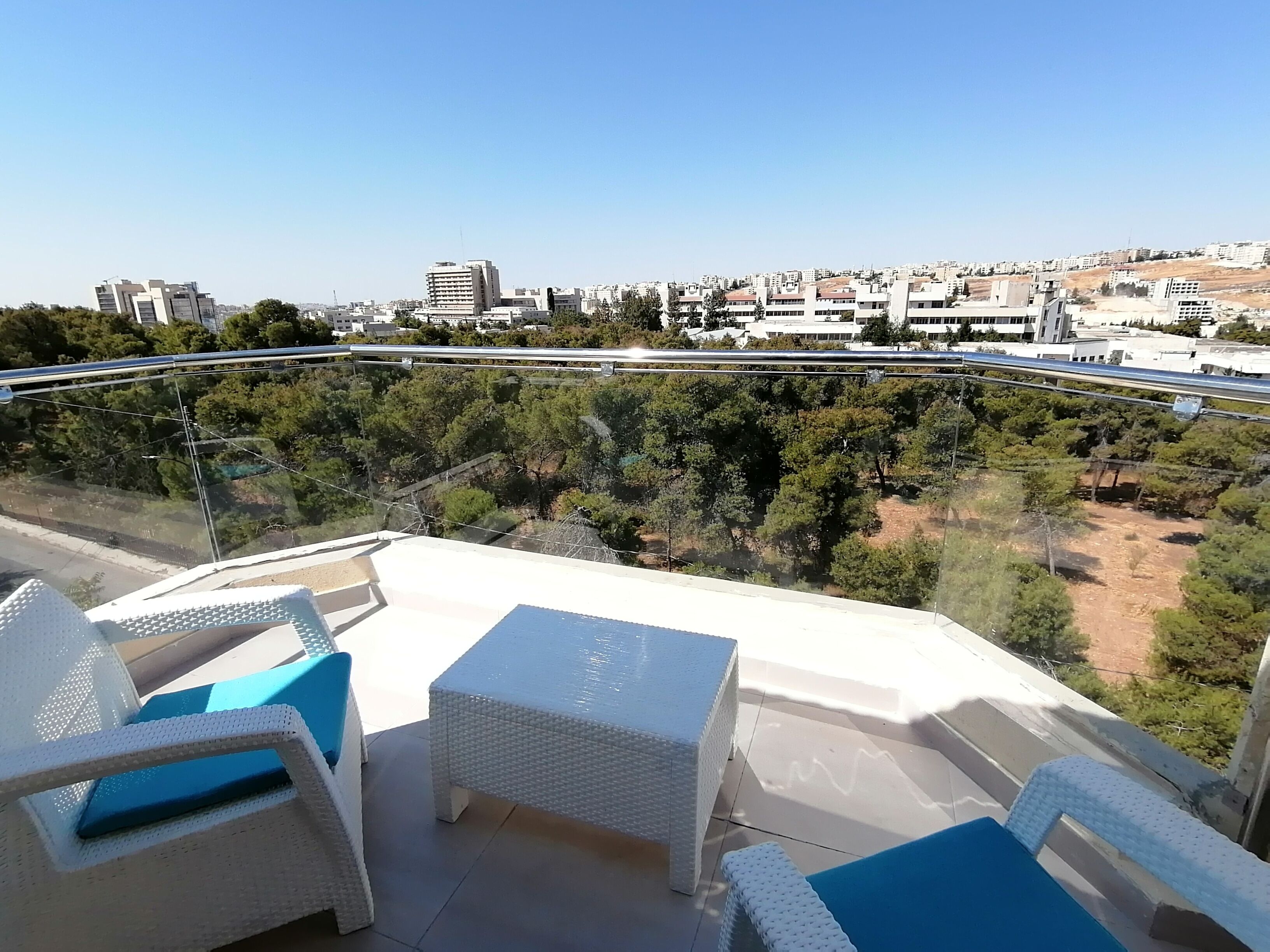 A balcony with white wicker furniture and a clear view of the cityscape.